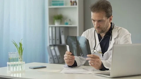 Attentive surgeon looking at bone x-ray and sending e-mail to patient on laptop Stock-Footage 82465468
