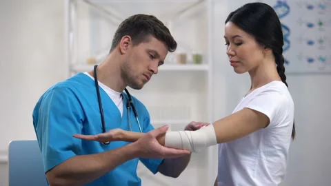 Attentive therapist fixing elbow elastic warp female patient after injury health Stock Footage 108499495