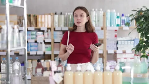 Attentive young female client scrolling phone while looking for something in Stock Footage 335613659