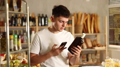 Attentive young guy is scanning QR code on whiskey bottle in grocery store Stock Footage 313457610