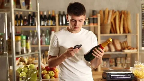 Attentive young guy is scanning QR code on spark wine bottle in grocery store Stock Footage 313874859