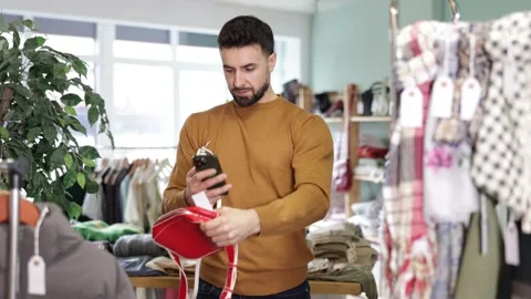 Attentive young man scanning barcode on handbag during shopping in clothing Stock Footage 343162464