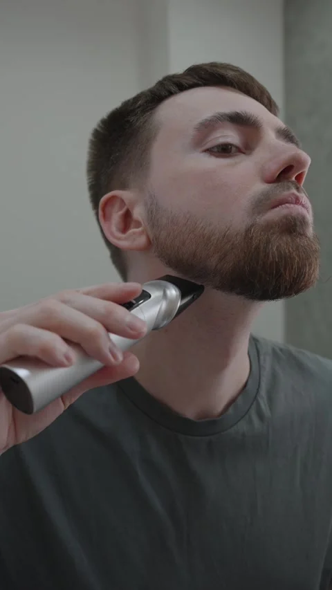 Attentively carving out precise borders of beard in mirror during grooming Stock Footage 333332395
