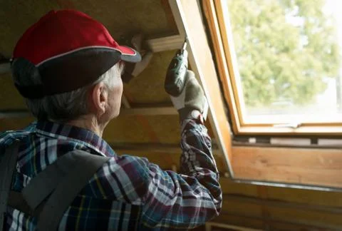 Attic insulation and renovation. Man fixing metal frame using an electric scr Stock Photos