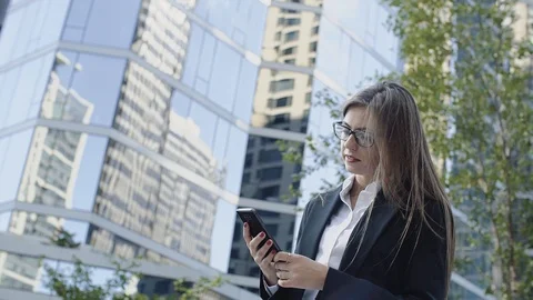 Attractive 30s lady in dark jacket with phone on the background of high Stock Footage 101083999
