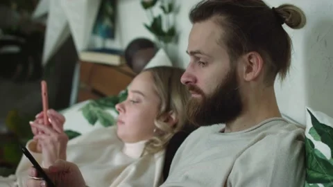 Attractive Affectionate Couple Relaxing Using Their Smartphones at home in bed. Stock Footage 147035926