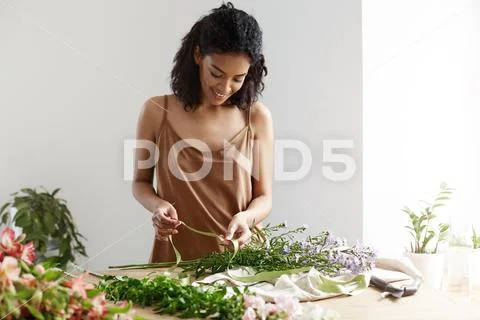 Attractive african female florist smiling holding green ribbon working with Stock Photos