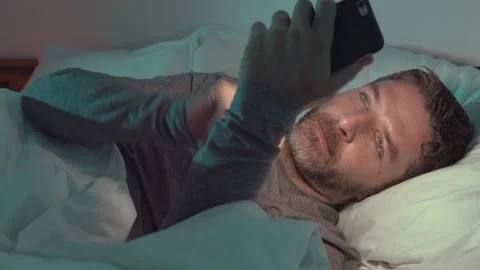 Attractive and happy man using mobile phone lying on bed at home Stock Footage 132313208