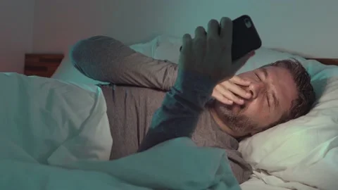 Attractive and happy man using mobile phone lying on bed at home Stock Footage 132313342