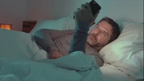 Attractive and happy man using mobile phone lying on bed at home Stock Footage 132313947
