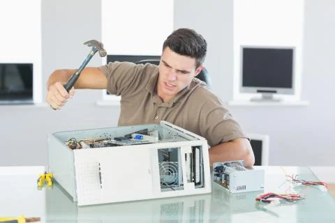 Attractive angry computer engineer destroying computer with hammer Stock Photos