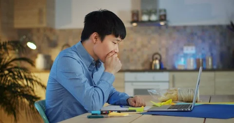 Attractive Asian student guy using computer studying online making notes with Stock Footage 124326212