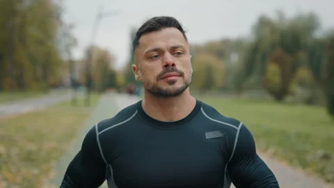Attractive athletic man jogging through the park. A man in slow-motion running Stock Footage 268383255