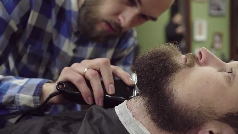 Attractive bearded man getting his beard shaved by modern barber in barber shop Stock Footage 69987460