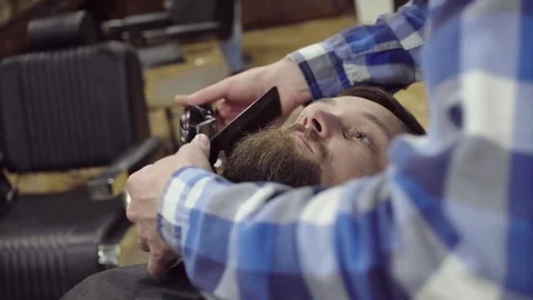 Attractive bearded man getting his beard shaved by modern barber in barber shop Stock Footage 69987562