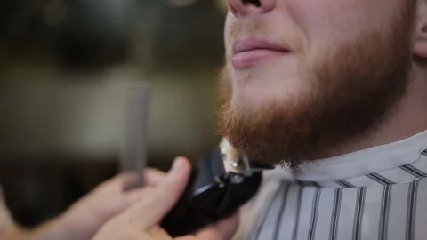 Attractive bearded man getting his beard shaved by modern barber in barber shop Stock Footage 93526058