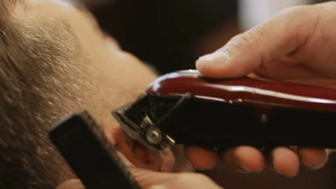 Attractive bearded man getting his beard shaved by modern barber in barber shop Stock Footage 102154307