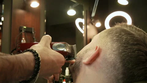 Attractive bearded man getting his beard shaved by modern barber in barber shop Stock Footage 102154354