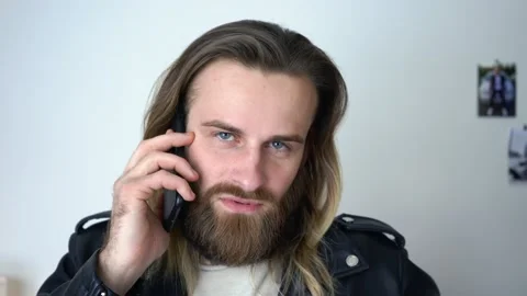 Attractive bearded man in leather jacket is talking on smartphone Stock Footage 147898656