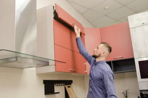 Attractive bearded man opens the top cabinet drawer in a modern kitchen Stock Photos