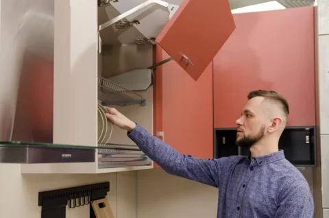 Attractive bearded man pulls out a plate from a drying cupboard in a modern k Stock Photos