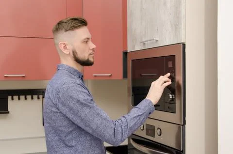 Attractive bearded man sets microwave oven timer in modern kitchen Foto stock