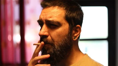 Attractive bearded man smokes a joint of weed in slow motion. Stock Footage 157486604
