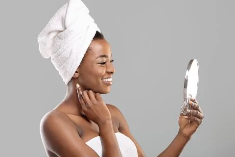Attractive black woman holding mirror and touching her perfect soft skin Stock Photos