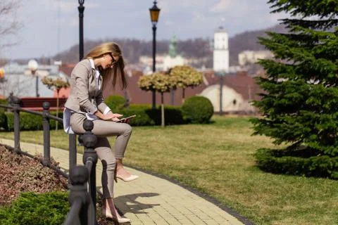 Attractive blonde businesswoman in the park. Woman holding tablet and wearing Stock Photos