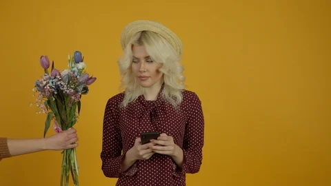 Attractive blonde girl in hat typing on smartphone and refusing tulip bouquet Stock Footage 125495053