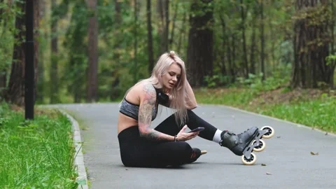 Attractive blonde relaxes while roller skating. She sits on the bike path and Stock Footage 312815611