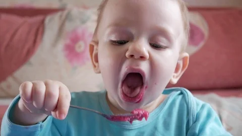 An attractive boy 2 years old eats a red beet salad. The face is smeared with Stock Footage 73838747