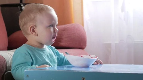 An attractive boy 2 years old eats a red beet salad. The face is smeared with Stock Footage 73839381