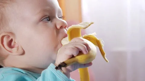 An attractive boy 2 years old eats a banana. Sits at the table at home Stock Footage 73840501