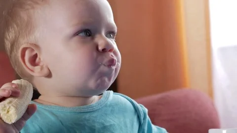 An attractive boy 2 years old eats a banana. Sits at the table at home Stock Footage 73840806