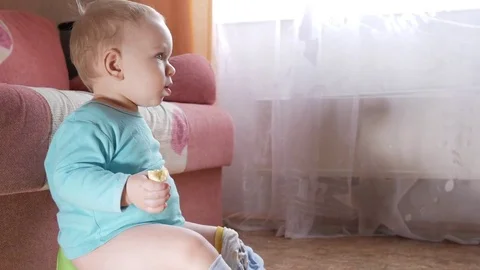 An attractive boy 2 years old sits on a pot at home and eats a banana. Looks Stock Footage 73841097