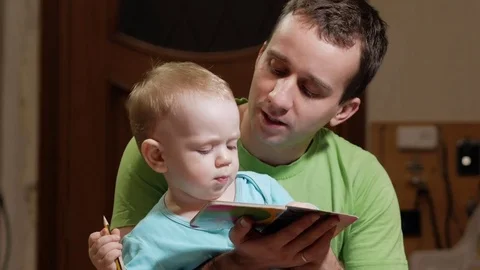 An attractive boy 2 years old and father read a book at home. Dad shows the Stock Footage 73843931