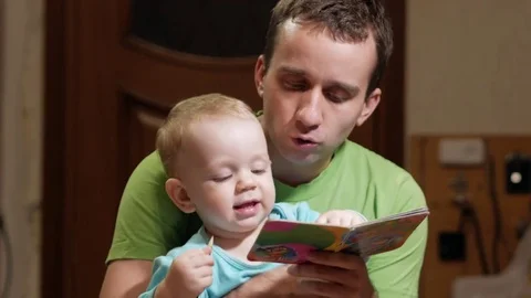 An attractive boy 2 years old and father read a book at home. Dad shows the Stock Footage 73844259