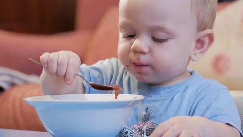 An attractive boy 2 years old is eating red soup himself. Spoon and hands Stock Footage 73965695