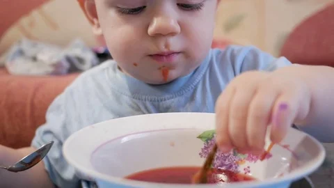 An attractive boy 2 years old is eating red soup himself. The bay leaf caught in Stock Footage 73966634