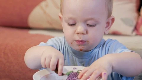 An attractive boy 2 years old is eating red soup himself. The bay leaf caught in Stock Footage 73966865