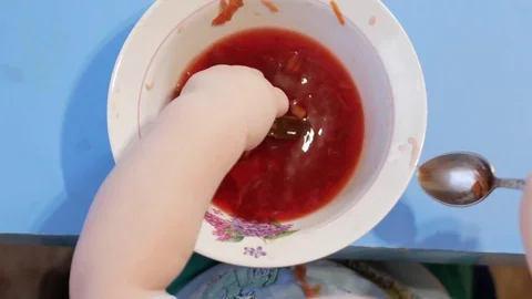 An attractive boy 2 years old is eating red soup himself. He climbs his hands in Stock Footage 73967001