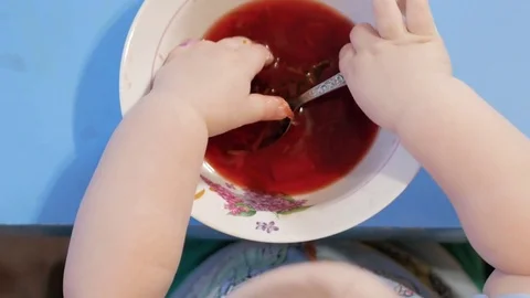 An attractive boy 2 years old is eating red soup himself. He climbs his hands in Video stock 73967144