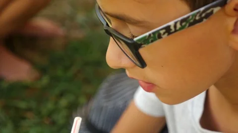 An attractive boy is drinking a drink through a straw, sitting on the grass Stock-Footage 80396603