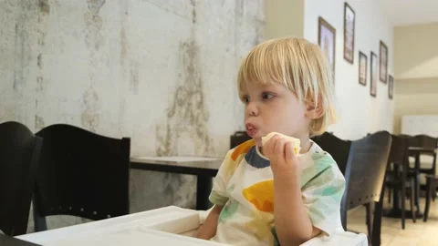An attractive boy eats a banana. Sits at the table at restaurant. Carefully Stock Footage 201461198