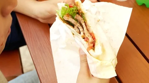 An attractive boy eats a fresh bread pita with a salad of fresh vegetables and Stock Footage 80422511
