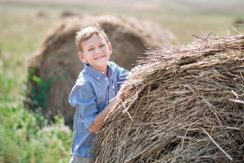 Attractive boy sitting on a haystack and smiling Stock Photos