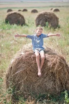 Attractive boy sitting on a haystack and smiling Fotos Stock
