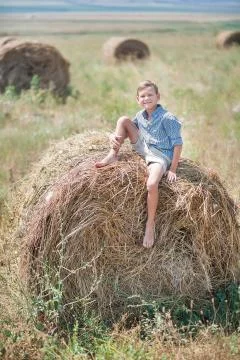 Attractive boy sitting on a haystack and smiling Stock-Fotos