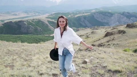 Attractive brunette in a hat and white shirt is enjoying nature in the mountains Stock Footage 131281846